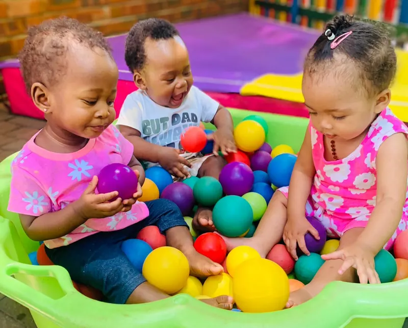 Three toddlers playing in a ball pit full of coloured balls