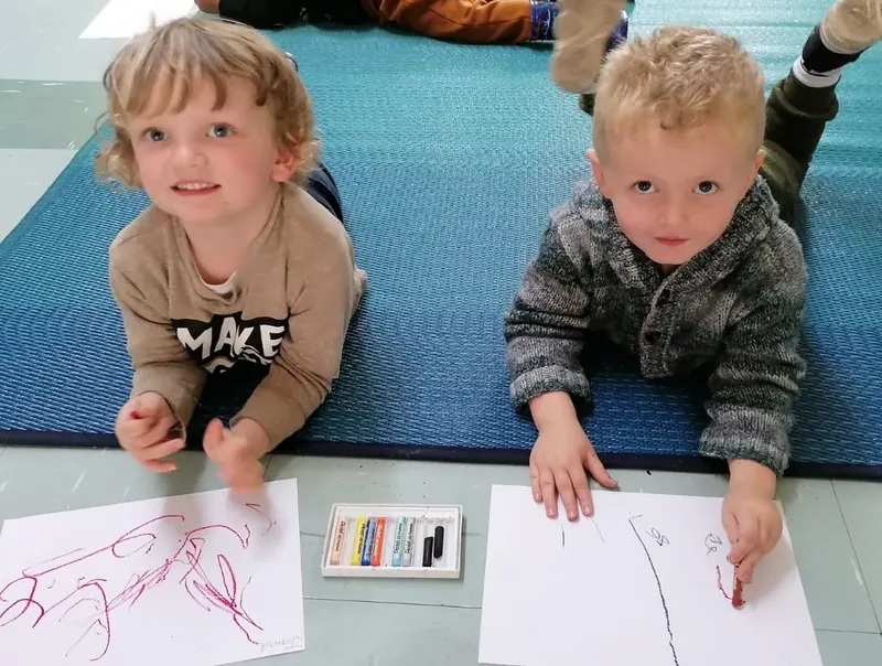 Two children drawing with crayons on paper at floor level