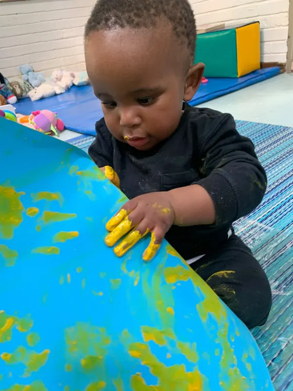 A toddler finger-painting in blue and yellow
