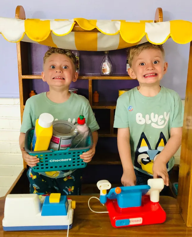 Two children behind a toy shop counter with baskets and a till