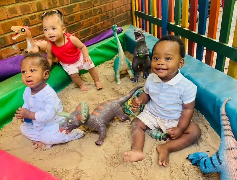 Toddlers playing with dinosaur toys in an indoor sandpit