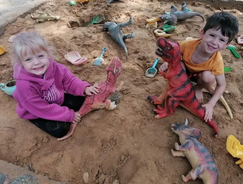 Two children digging for dinosaurs in the sandpit