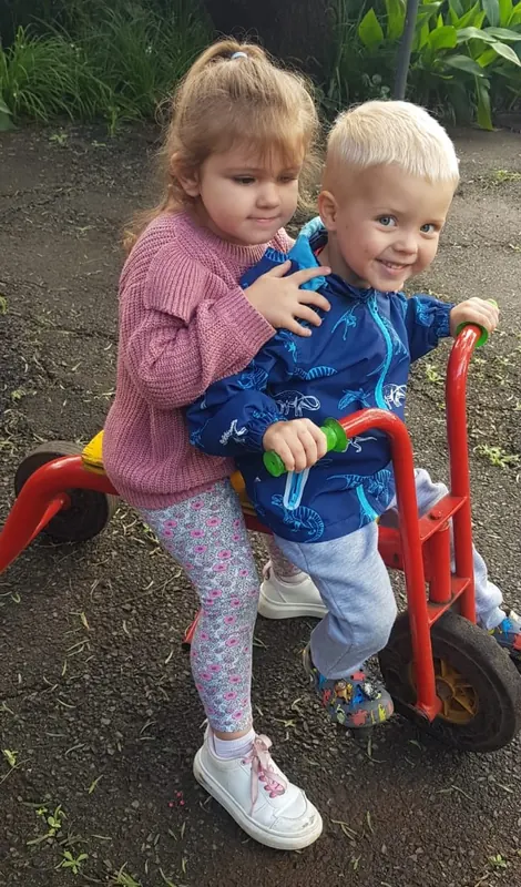 Two children sharing a trike on the garden path
